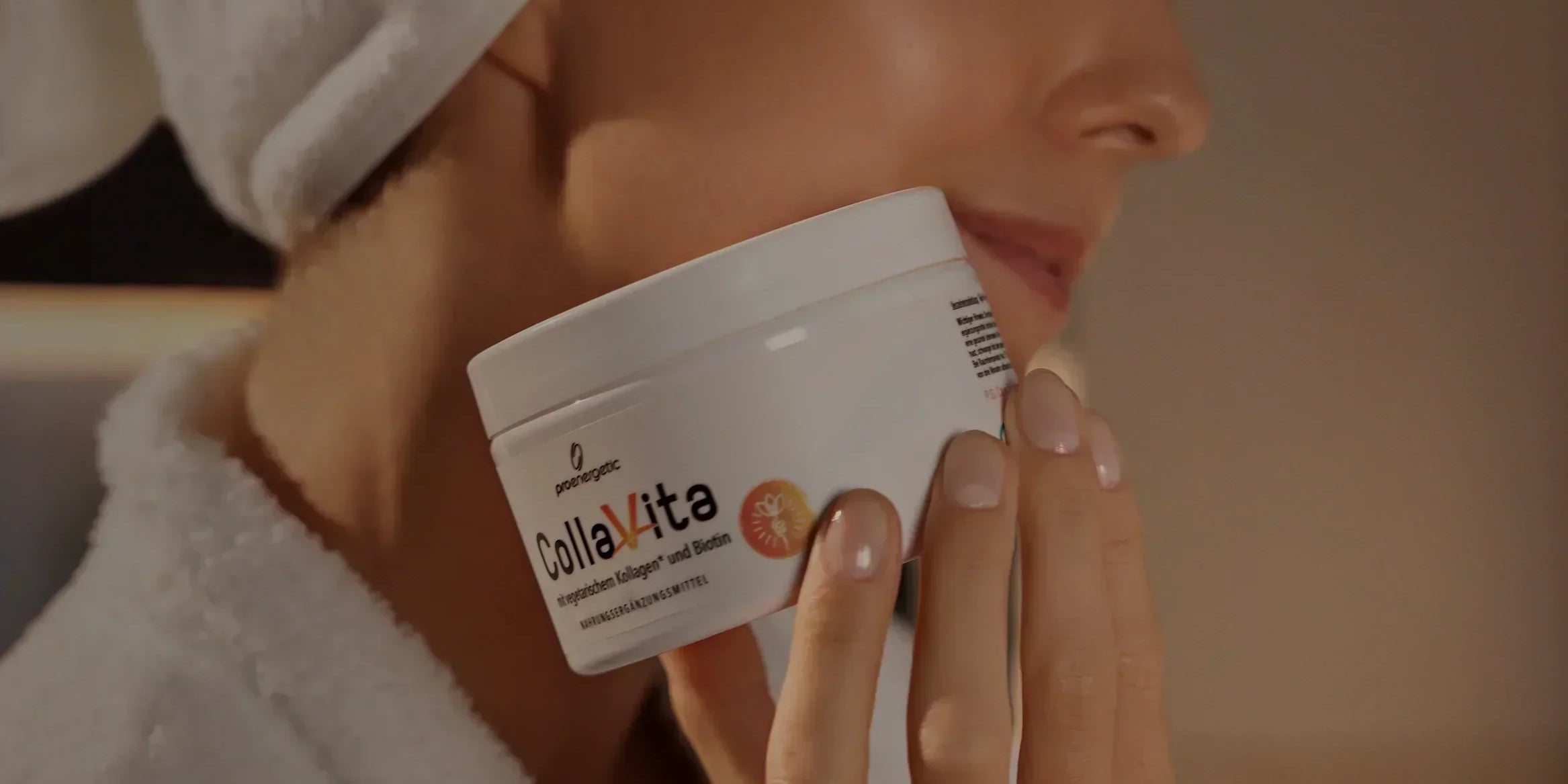 Frau mit weißem Handtuch auf dem Kopf hält Kollagen-Supplement-Glas nah an ihrem Gesicht