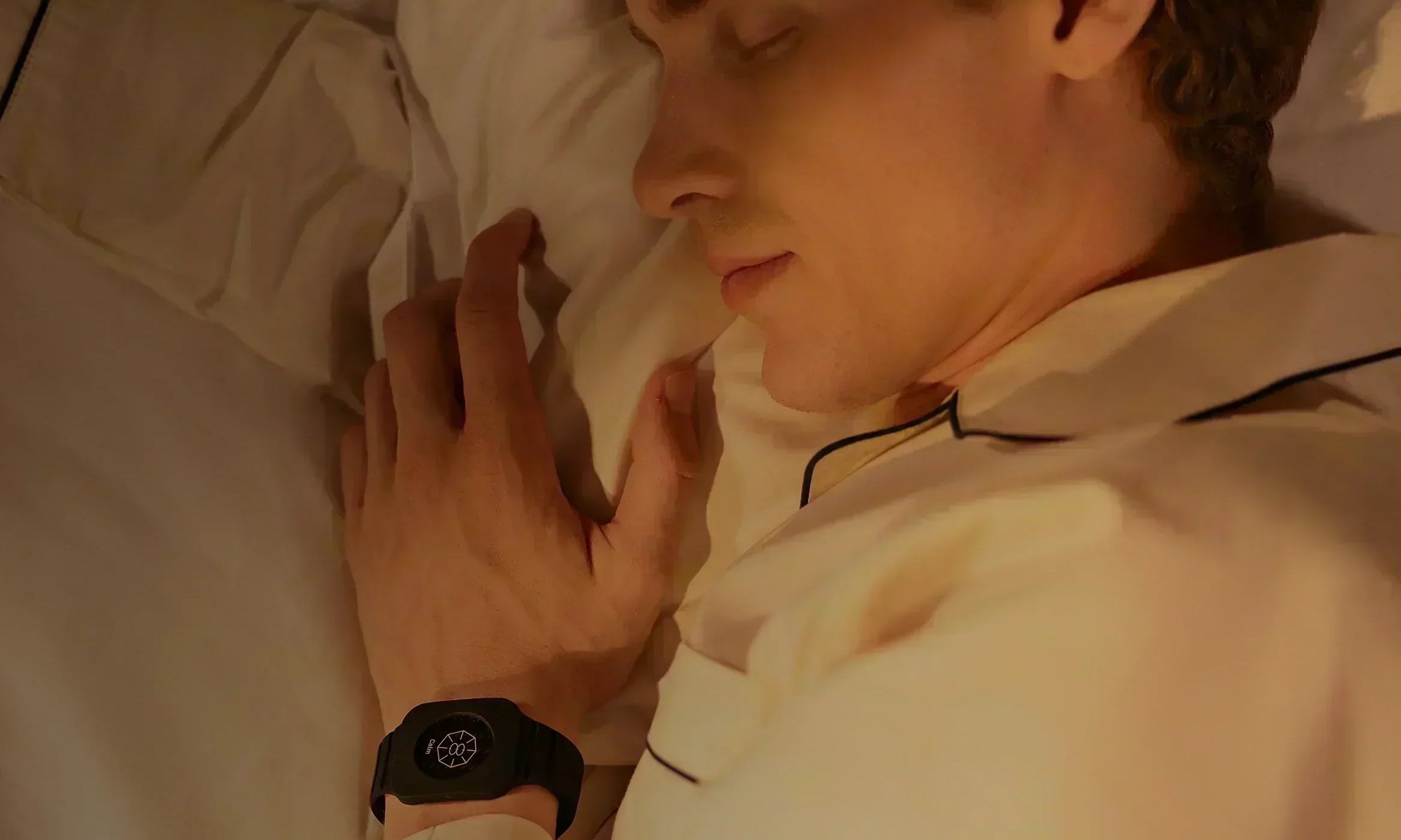 Mann liegt schlafend im Bett bei warmem Licht mit geschlossenem Augen und trägt Eloop Band mit Calm Chip am Handgelenk