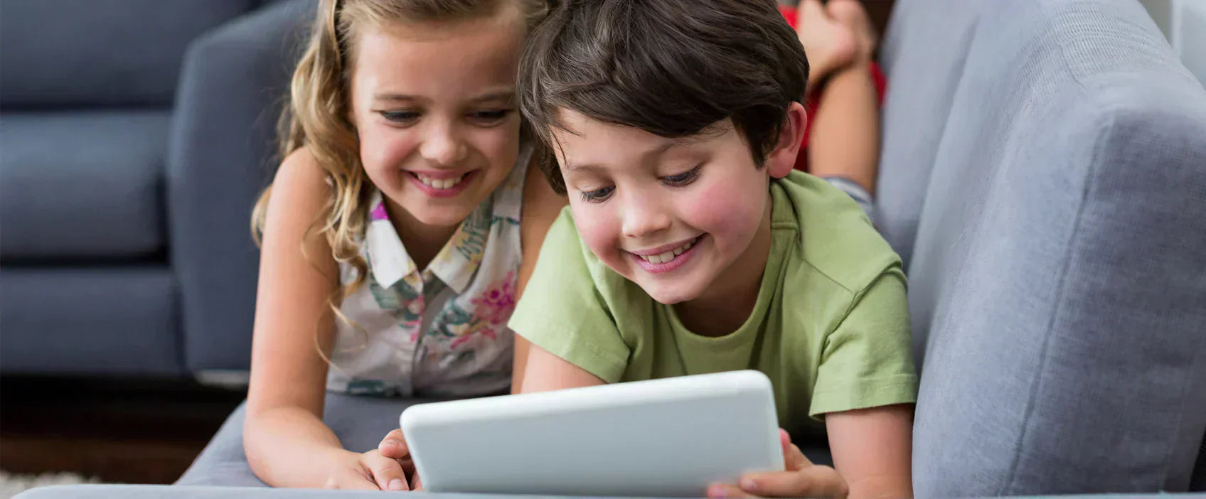 Zwei Kinder sitzen nebeneinander und schauen auf ein Tablet  