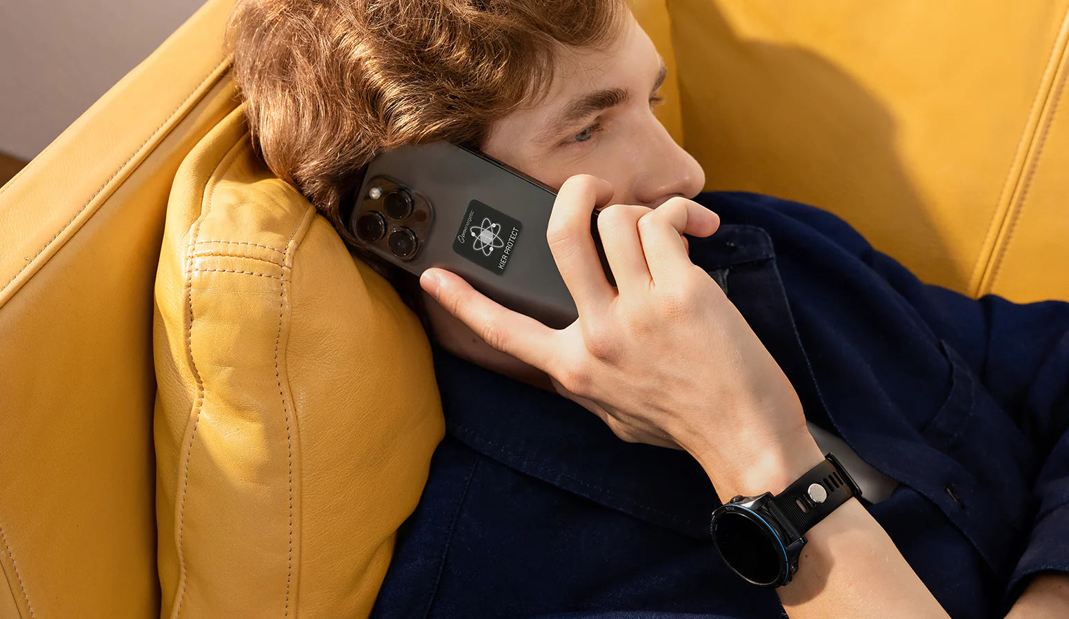 Mann liegt im Innenraum auf einem Sofa und telefoniert mit einem Smartphone mit angebrachtem KIER Protect Mobile Element