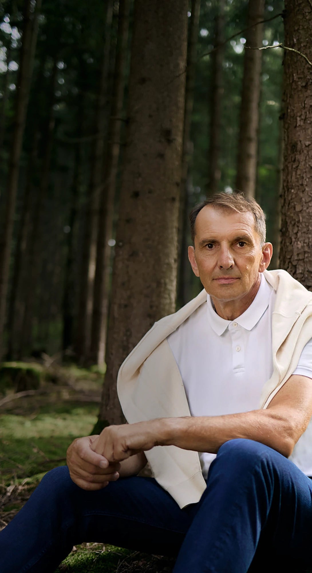 Mann sitzt im Wald an Baumstamm in natürlicher Umgebung bei Tageslicht