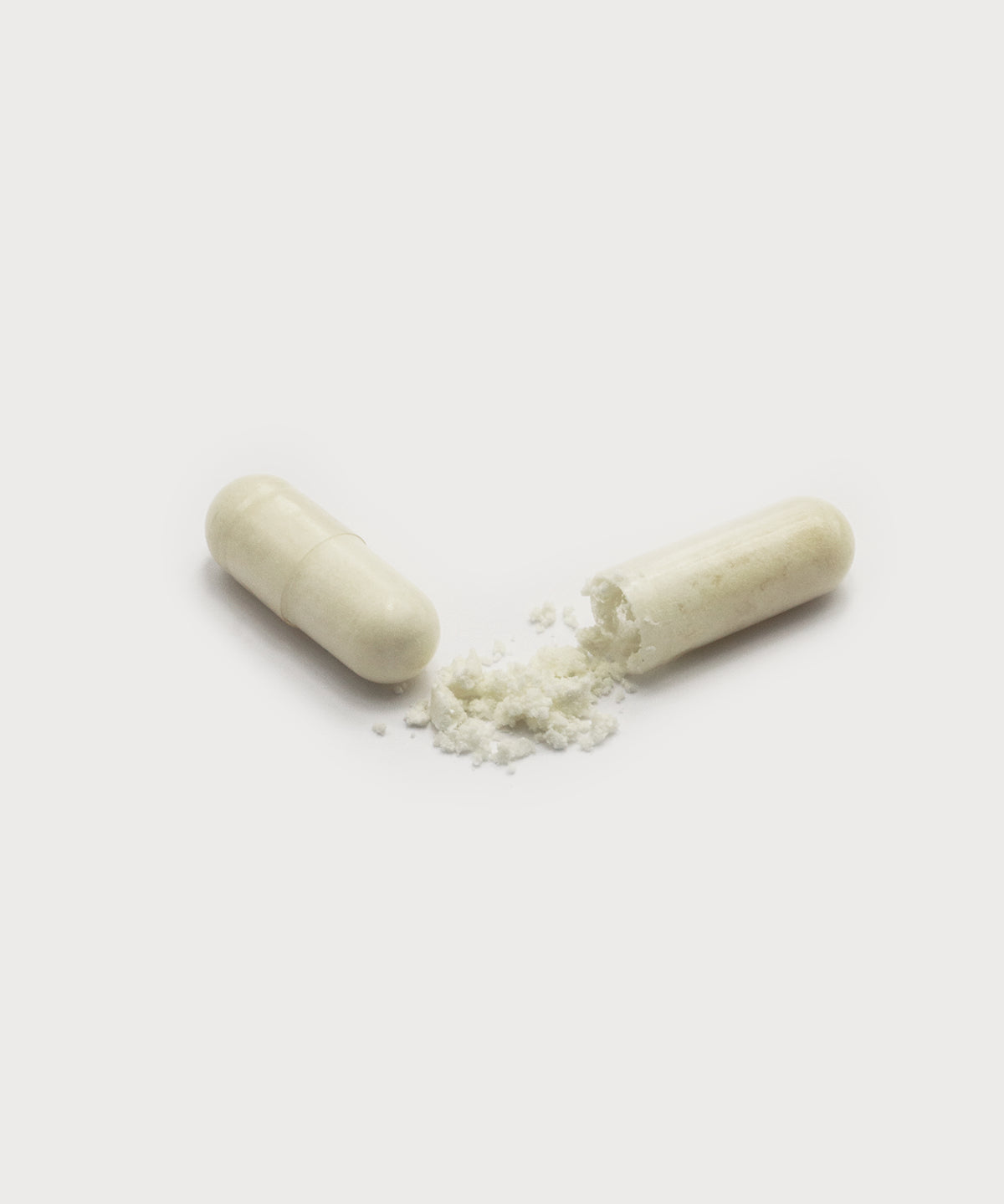 Geöffnete Amino-Caps-Kapsel mit ausgetretenem, hellem Pulver neben einer geschlossenen Kapsel, freigestellt vor hellem, neutralem Hintergrund.