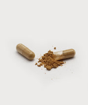 Eine geschlossene und eine geöffnete Kapsel mit braunem Pulver auf hellem Hintergrund, Pulver lose zwischen den Kapselhälften.