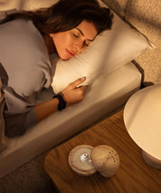 Dormea auf seinem natürlichen Sandstein auf einem Nachttisch neben einer Frau, die friedlich im Bett schläft.
