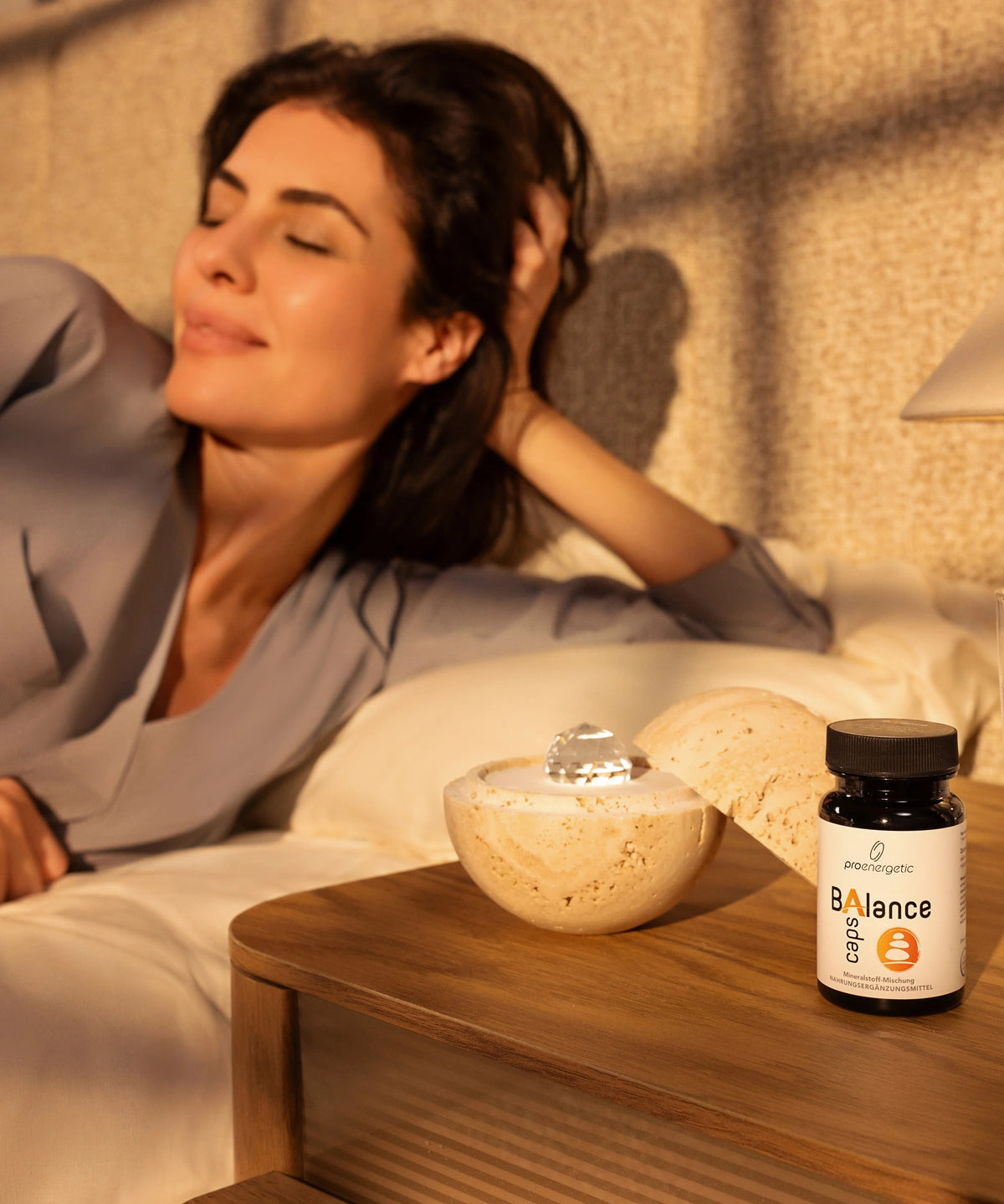 Eine Frau, die sich im Bett entspannt, neben ihr auf dem Nachttisch die Nahrungsergänzungsmittel Dormea und ProEnergetic Balance Caps.