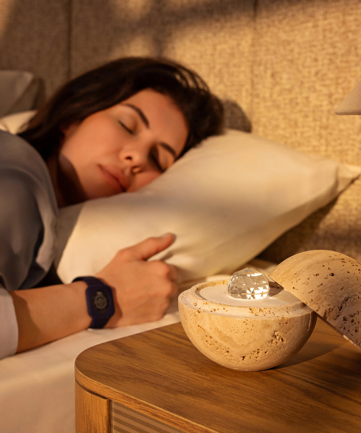 Eine Frau schläft friedlich, während sie das Eloop-Band mit sleep-Chip trägt; auf dem Nachttisch steht der Dormea aus natürlichem Sandstein.