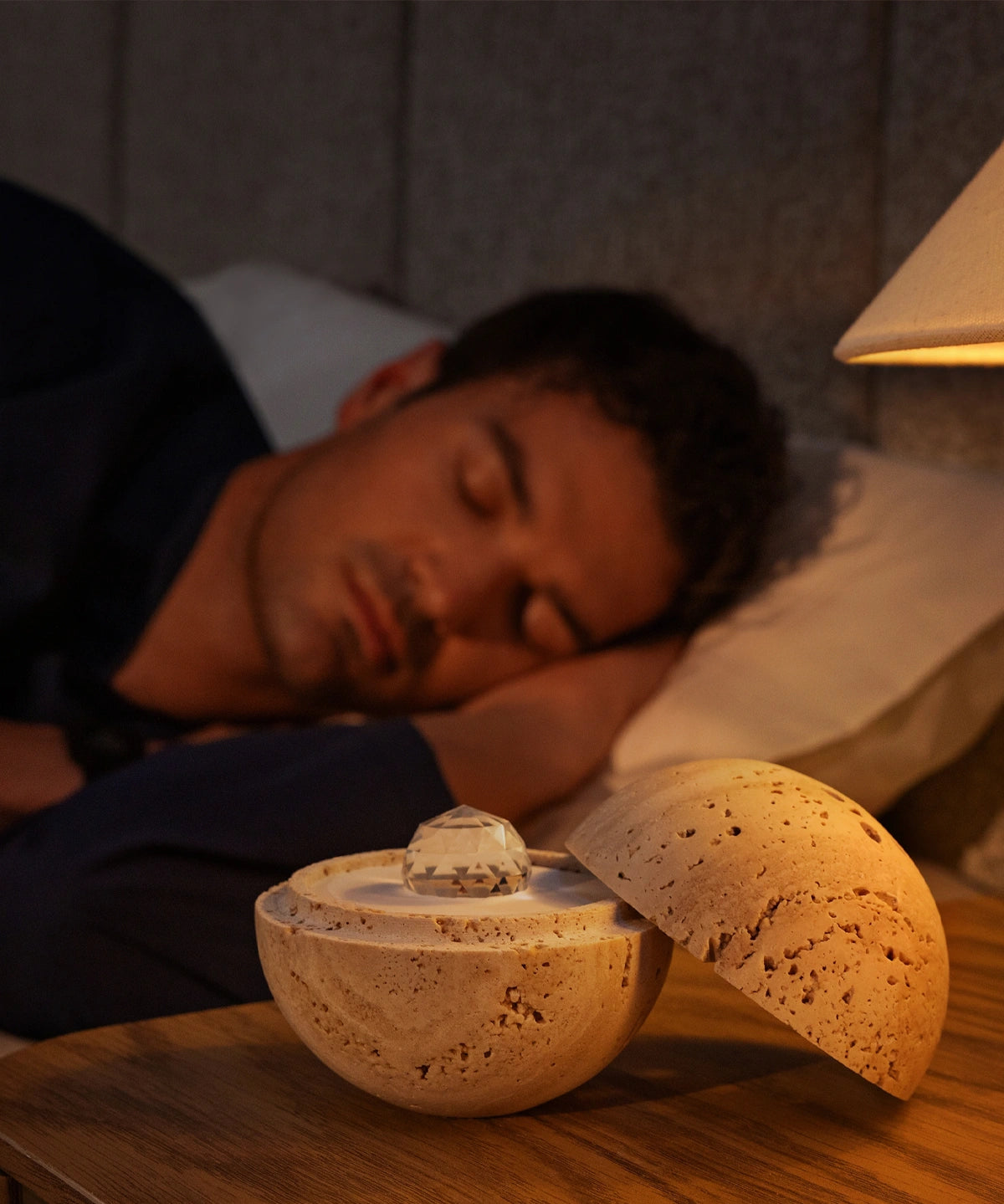 Der Dormea aus Sandstein auf einem Nachttisch, während im Hintergrund ein Mann friedlich schläft.
