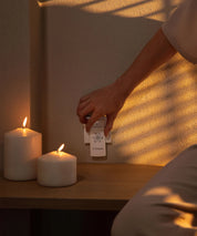 Hand greift im Innenraum nach einem eingesteckten E-Protect S90 Steckelement in einer Wandsteckdose neben brennenden Kerzen