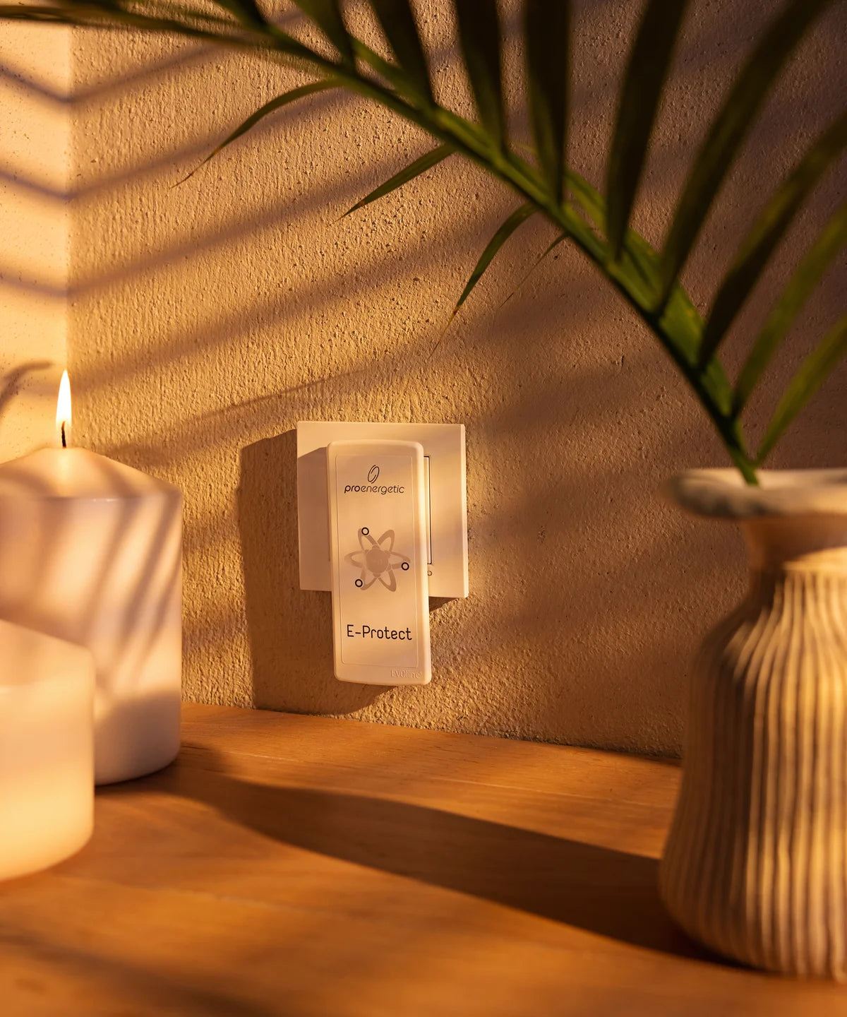 E-Protect S90 Steckelement ist in einer Wandsteckdose im Innenraum eingesteckt, umgeben von Kerze und Pflanze auf einem Holzregal