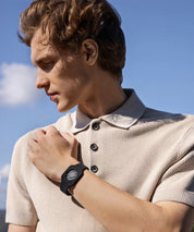 Person steht im Freien und trägt ein schwarzes Eloop Band Silikonarmband mit Ground Chip am Handgelenk, blickt zur Seite vor blauem Himmel