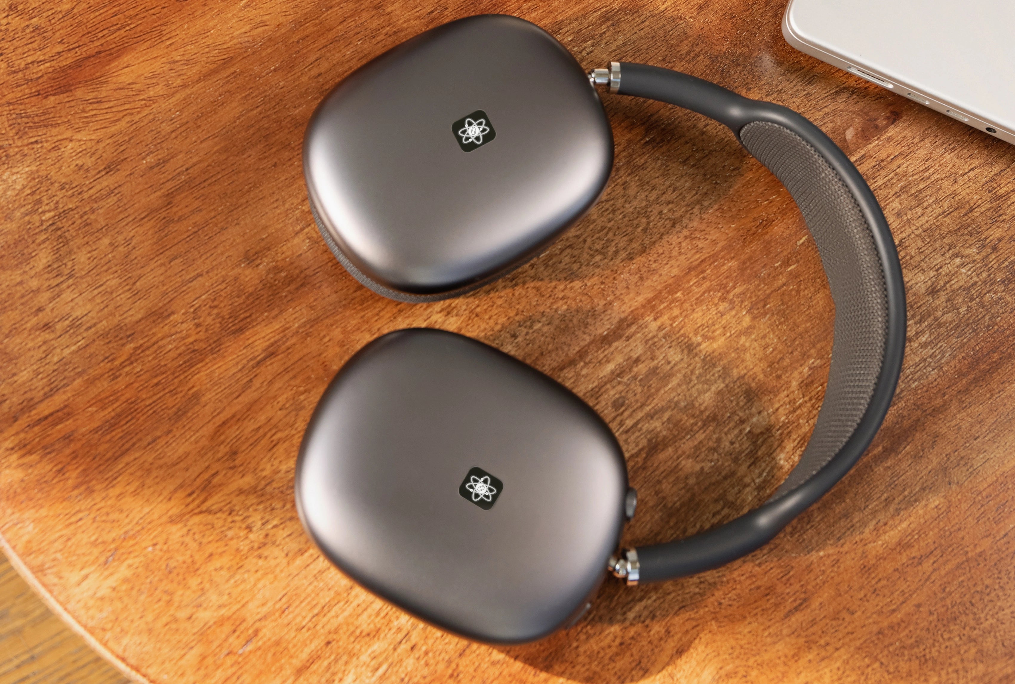 Graue Over-Ear-Kopfhörer liegen auf einem Holztisch, auf beiden Ohrmuscheln ist ein E-Protect-Audio-Aufkleber sichtbar.