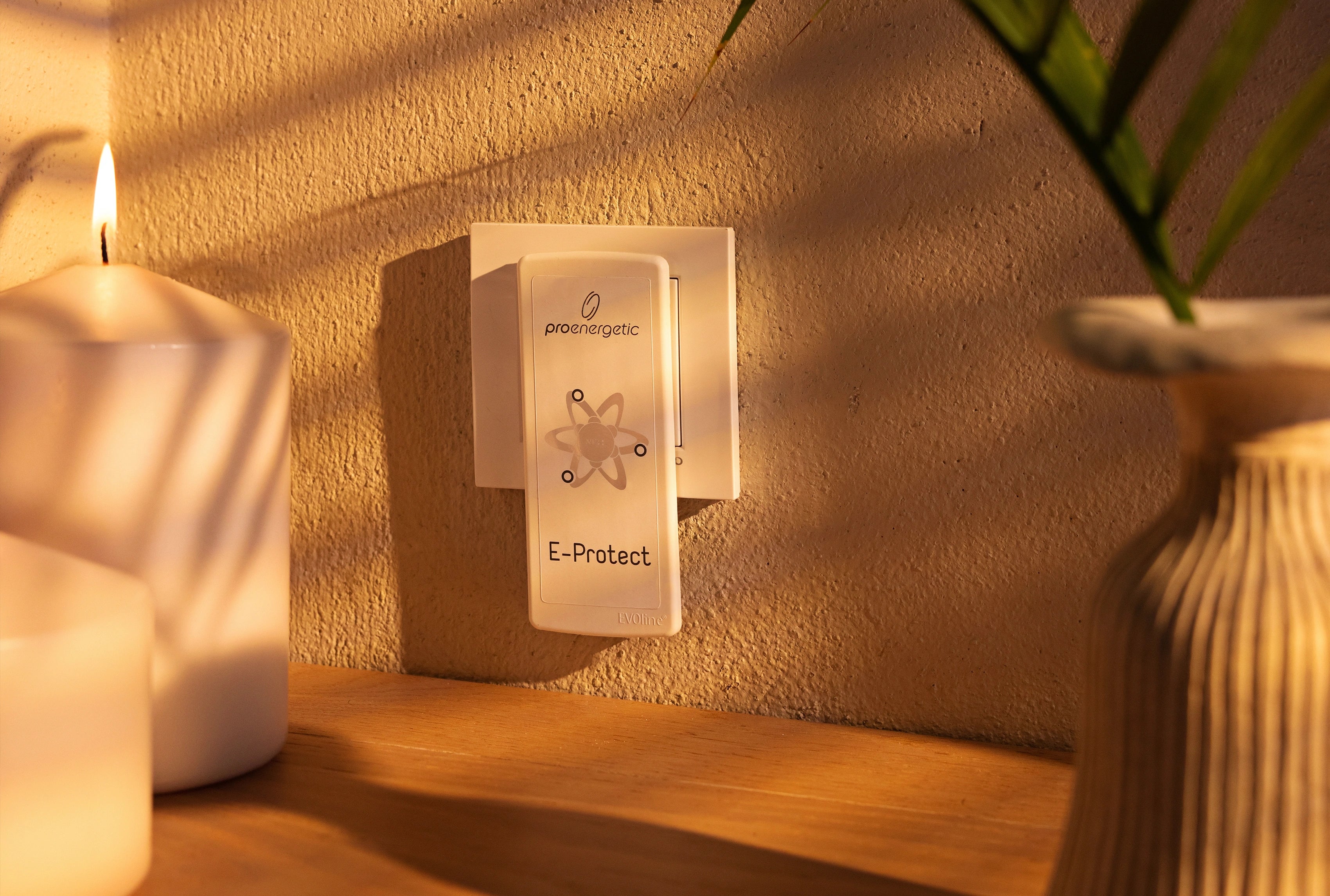 E-Protect S90 Steckelement ist in einer Wandsteckdose im Innenraum eingesteckt, umgeben von Kerze und Pflanze auf einem Holzregal