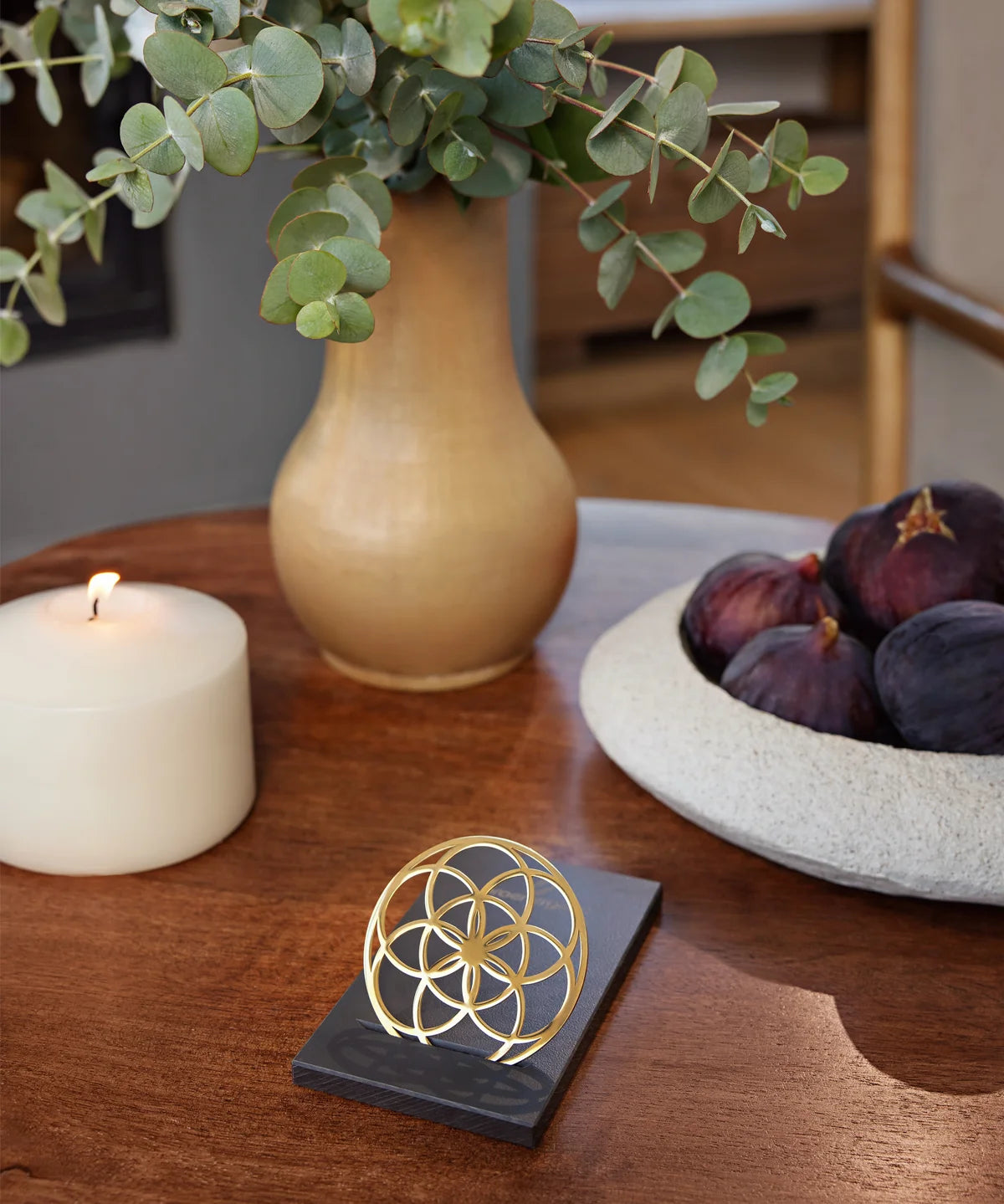 Flower of Love Goodie als goldenes Ornament auf schwarzem Sockel, arrangiert auf einem Holztisch in wohnlicher Umgebung
