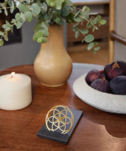 Flower of Love Goodie als goldenes Ornament auf schwarzem Sockel, arrangiert auf einem Holztisch in wohnlicher Umgebung