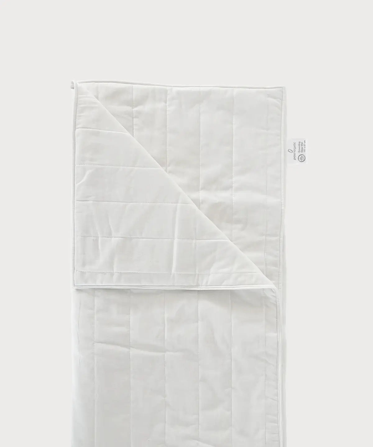 Weiße Grounding Sleep Mat mit gesteppter Oberfläche, teilweise aufgeklappt und mit sichtbarem Textiletikett auf hellem Hintergrund