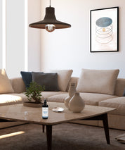 Harmony Spray in schwarzer Sprühflasche steht auf einem Couchtisch in einem hellen Wohnzimmer mit Sofa, Lampe und Wandbild