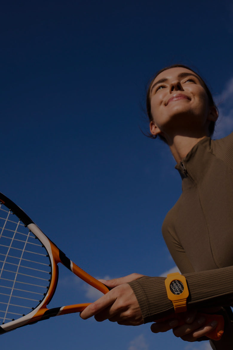 Frau mit Tennisschläger im Freien trägt ein orangefarbenes Eloop Band mit Move Chip vor blauem Himmel