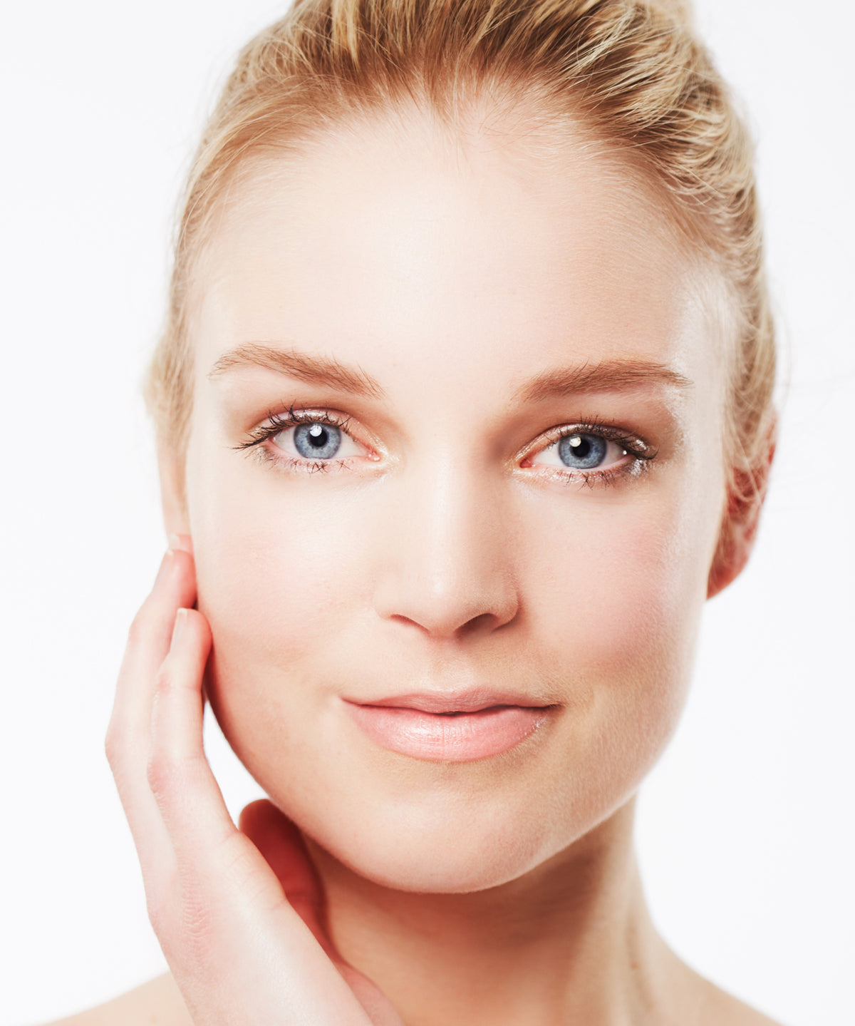 Porträt einer Frau mit ebenmäßiger, gepflegter Haut und natürlichem Make-up, die sanft ihre Wange berührt, vor hellem Hintergrund – Sinnbild für Schönheit, Pflege und Wohlbefinden.