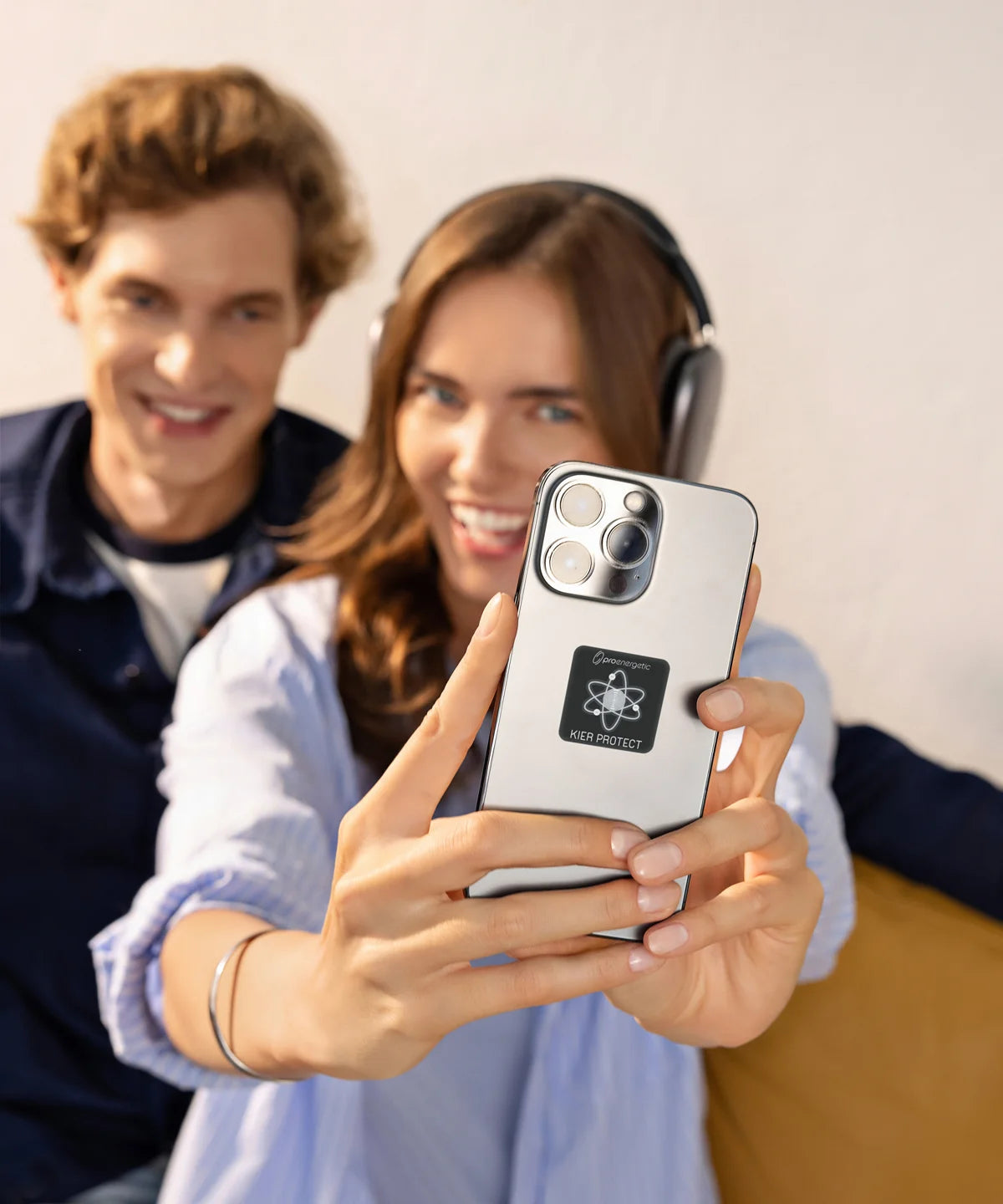 Zwei Personen sitzen im Innenraum, eine Frau hält ein Smartphone mit angebrachtem KIER Protect Mobile Element in die Kamera