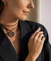 Detailaufnahme einer Frau im Innenraum mit getragener ProEnergetic KIER Protect Necklace am Hals, schwarzes Lederband und runder Anhänger sichtbar