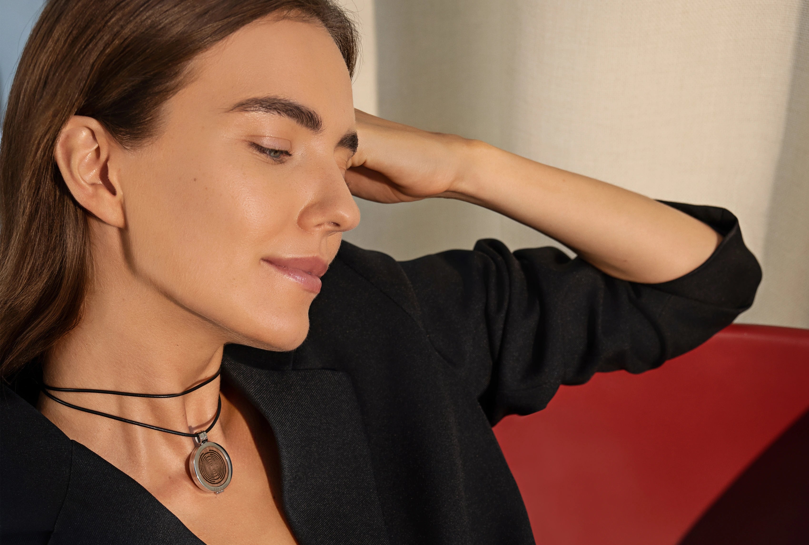 Frau im Innenraum trägt die ProEnergetic KIER Protect Necklace mit schwarzem Lederband und rundem Anhänger sichtbar am Hals