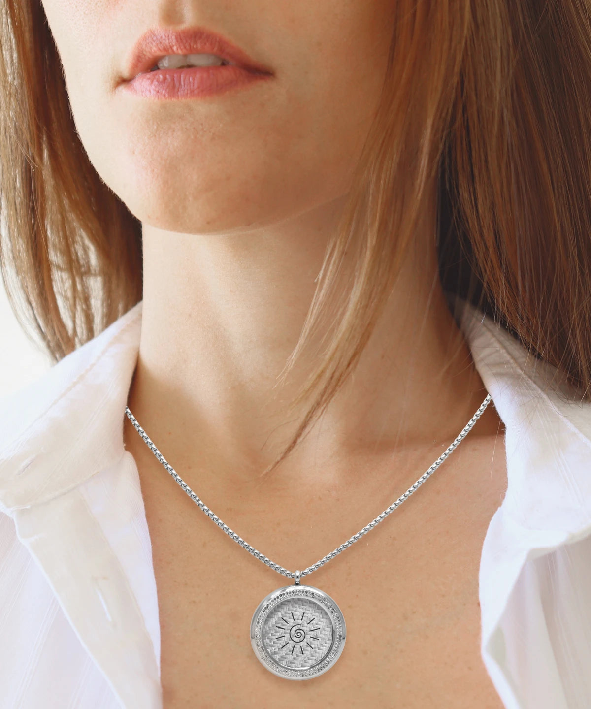 Frau trägt Love & Light Pendant von ProEnergetic, eine silberne Halskette mit rundem Anhänger und eingraviertem Symbol, kombiniert mit weißer Bluse in natürlichem Licht.