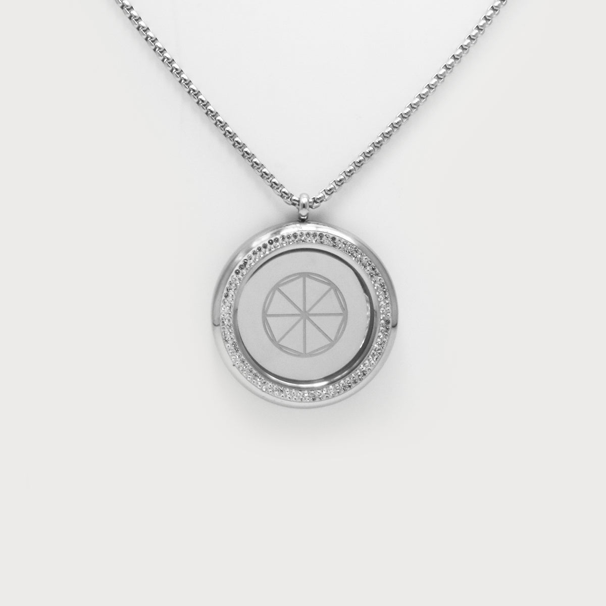 Love & Light Pendant. Silberner Rundanhänger mit feiner Kette, umlaufender Steinbesatz und mit geometrischem Symbol in der Mitte auf hellem Hintergrund.