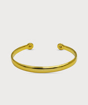 Goldfarbener Lunara Cuff Armreif mit glatter polierter Oberfläche und offenen Enden vor hellem Hintergrund
