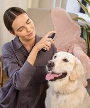 Frau sprüht „Pet Balance“ Aura Spray auf einen entspannten, hellen Hund im Wohnraum. Der Hund sitzt ruhig mit herausgestreckter Zunge, während die Frau das Spray aus kurzer Distanz anwendet. Helle, freundliche Atmosphäre mit Sofa und Pflanzen im Hintergrund.