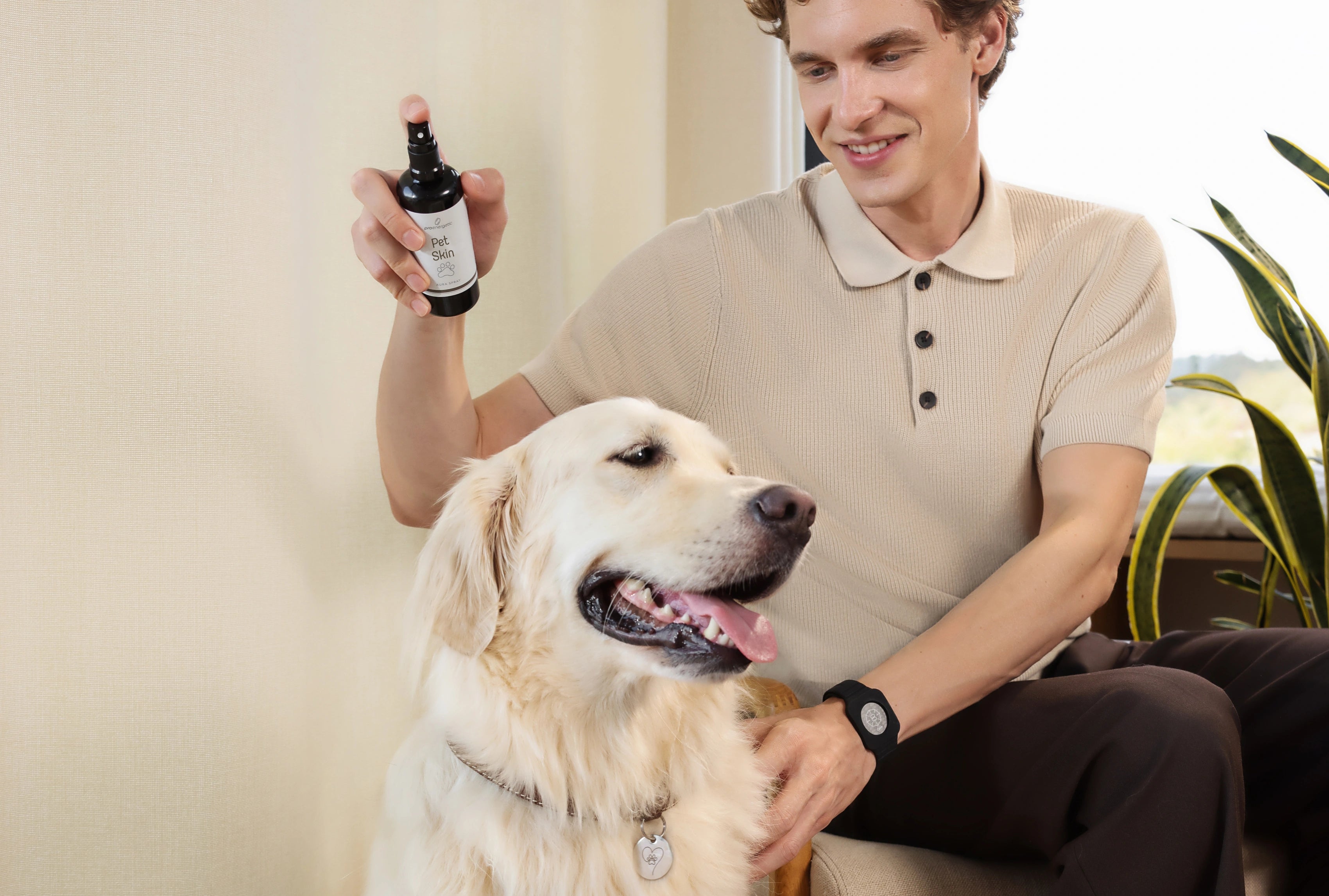 Mann sitzt entspannt neben einem Golden Retriever und sprüht „Pet Skin – Aura Spray“ von proenergetic auf das Fell des Hundes. Der Hund wirkt ruhig und zufrieden, die Szene ist hell, wohnlich und vermittelt Pflege sowie Wohlbefinden für Haustiere.