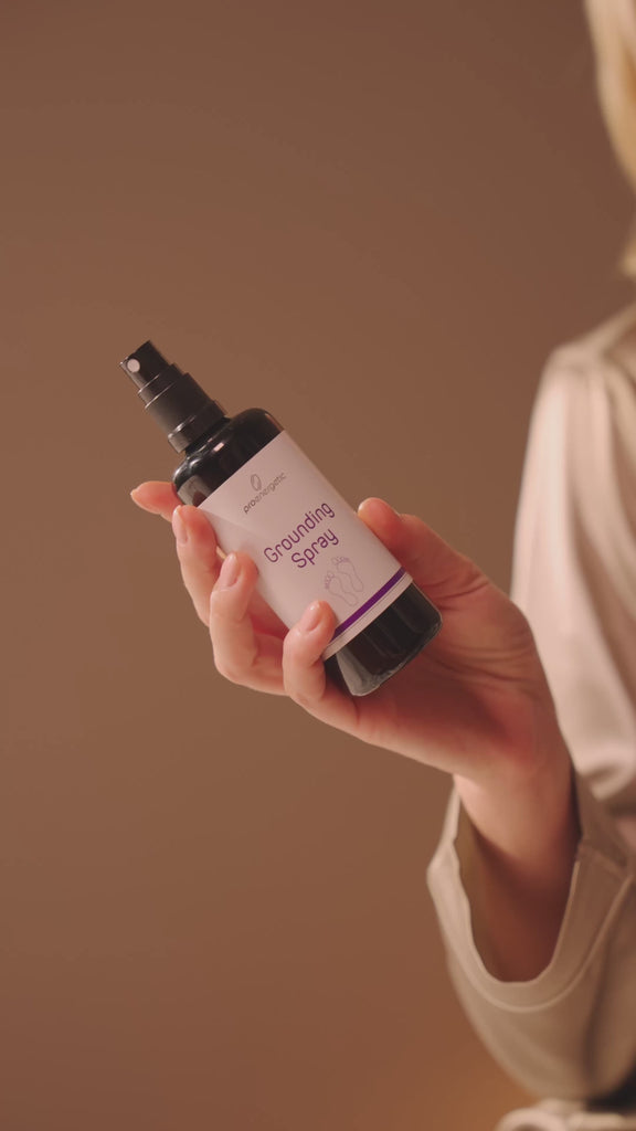 Person sitzt auf dem Bett, sprüht Grounding Spray auf den linken Fuß und schlüpft anschließend mit beiden Füßen in Hausschuhe