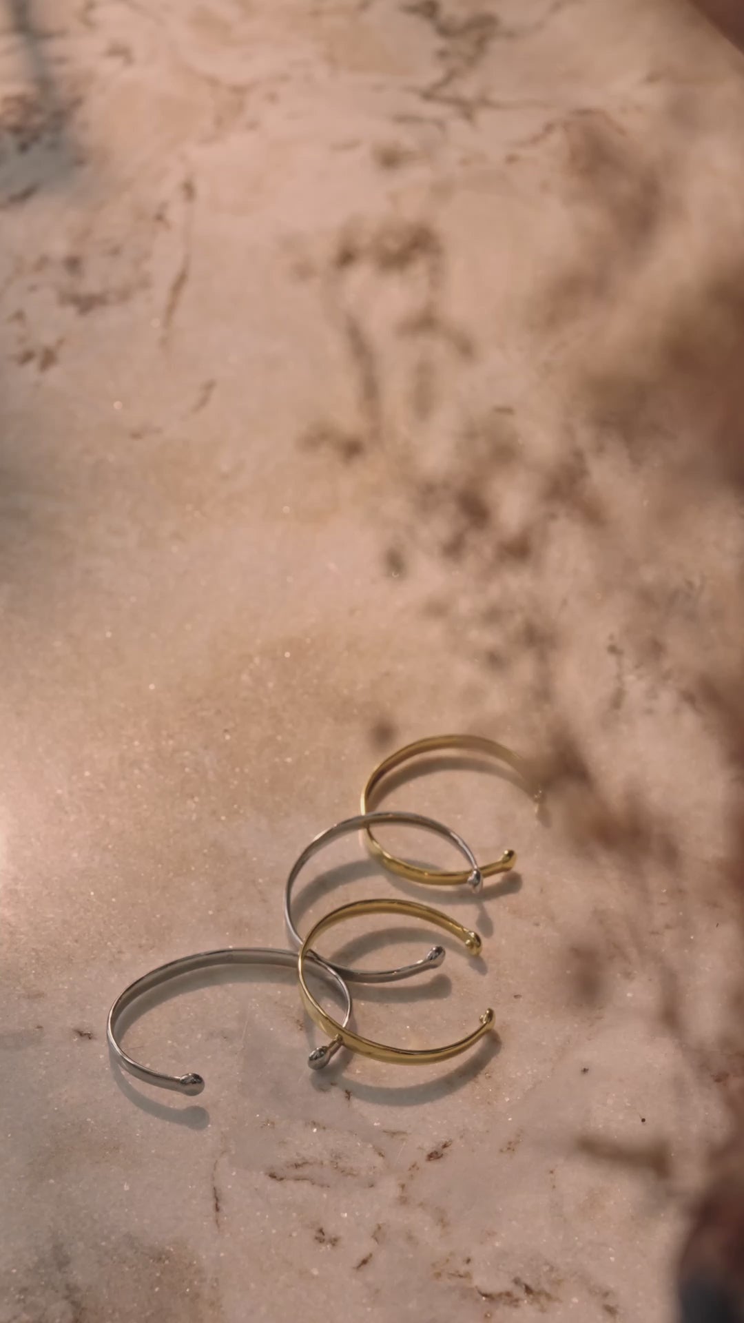 Vier Lunara Cuff Armreifen liegen nebeneinander auf hellbraunem Untergrund in abwechselnder Farbreihenfolge, zwei in Gold und zwei in Silber