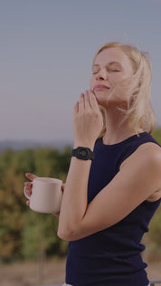 Person trinkt aus einer Tasse im Freien und trägt ein schwarzes Eloop Band Silikonarmband mit Calm Chip am Handgelenk vor blauem Himmel