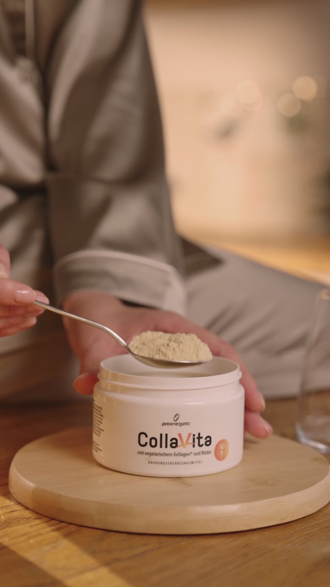 Person gießt ein gelbes Getränk aus einer Karaffe in ein Glas; davor steht eine geöffnete Dose CollaVita auf einem Holztisch. Person trinkt aus Glas. Video.