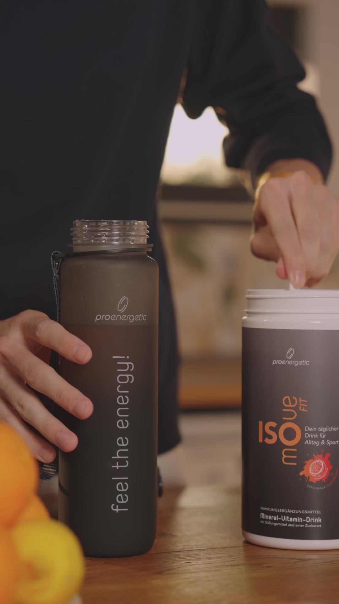 Person trinkt einen Elektrolytedrink aus der schwarzen Pure Move Trinkflasche in einem Innenraum bei warmem Licht