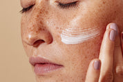 Nahaufnahme eines Gesichts mit aufgetragener weißer Creme auf der Wange und Hand beim Einmassieren.