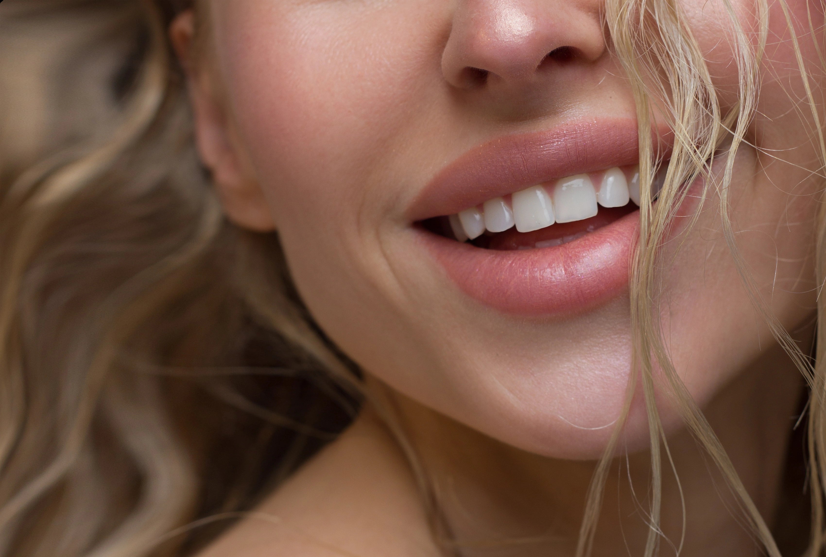 Nahaufnahme eines lächelnden Mundes mit gepflegten Lippen und sichtbaren Zähnen.