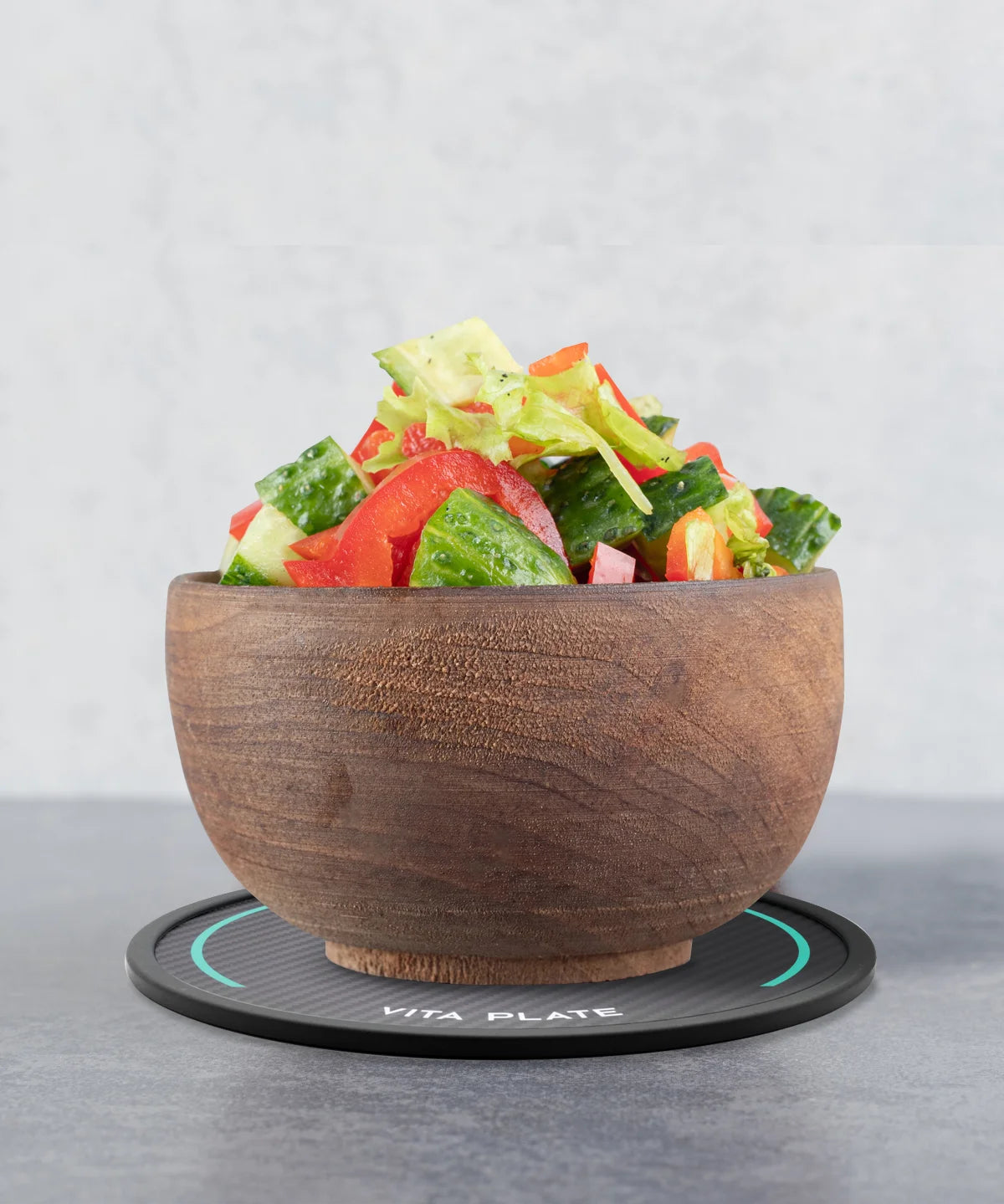 Holzschale mit gemischtem Salat steht auf der runden Vita Plate mit schwarzer Carbonoptik auf grauer Oberfläche
