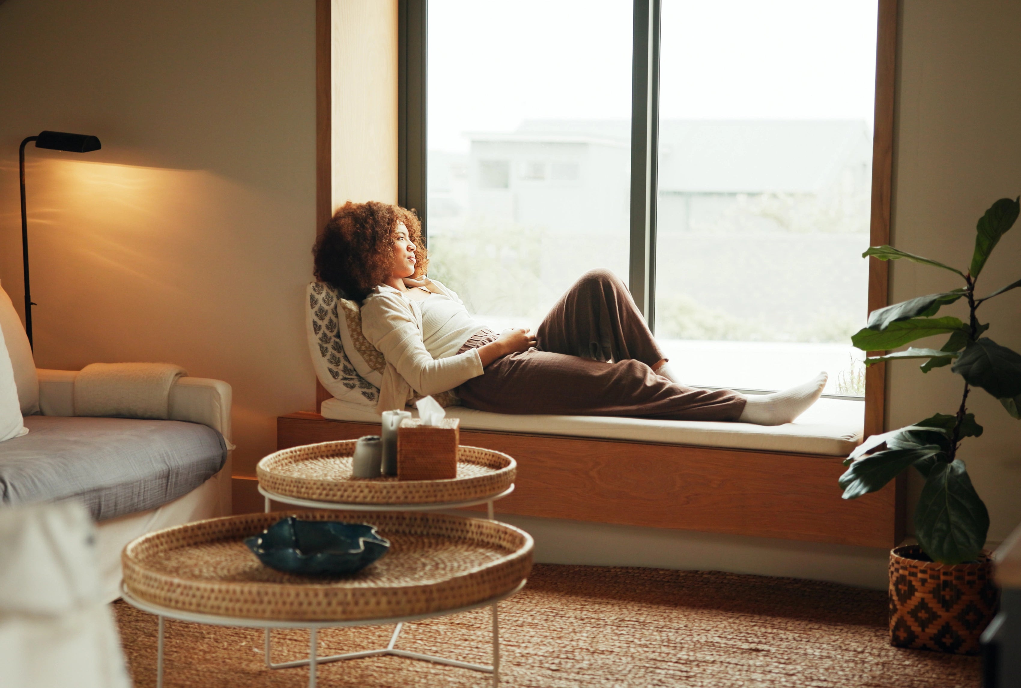 Frau liegt auf Fensterbank mit Kissen in modernem Wohnraum neben Pflanze.